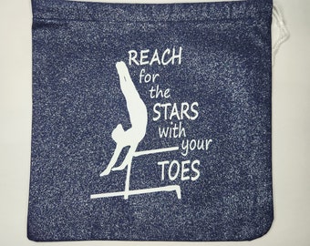 May include: A blue drawstring bag with a white silhouette of a gymnast on the uneven bars. The bag has the text "Reach for the stars with your toes" printed on it.