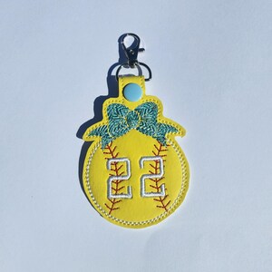 Puede incluir: Llavero de softball amarillo con un lazo azul y el n&uacute;mero 22 bordado.