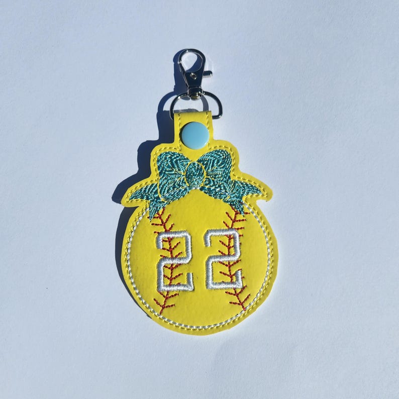 Puede incluir: Llavero de softball amarillo con un lazo azul y el n&uacute;mero 22 bordado.