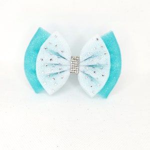 May include: A light blue and turquoise bow with a silver rhinestone center. The bow is made of tulle and has a sparkly finish.