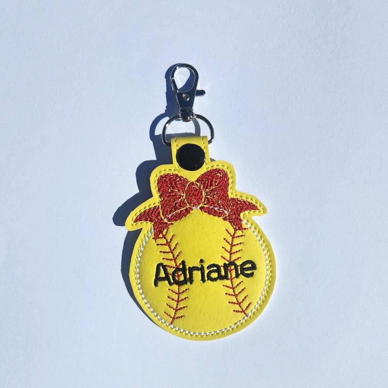 Puede incluir: Llavero de softball amarillo con un lazo rojo y el nombre Adriane bordado.