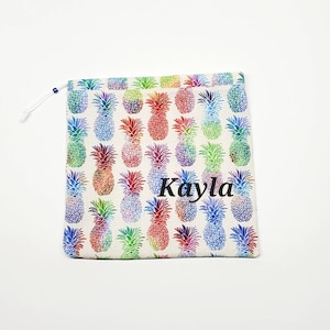 May include: A white drawstring bag with a colorful pineapple print and the name "Kayla" embroidered on the front.