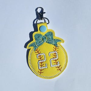 Puede incluir: Llavero de softball amarillo con un lazo azul y el n&uacute;mero 22 bordado.
