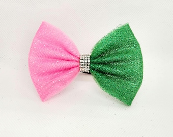 May include: A pink and green tulle bow with a rhinestone center. The bow is perfect for adding a touch of sparkle to any outfit.