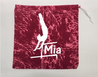 May include: Red and pink tie-dye drawstring bag with a white silhouette of a gymnast on uneven bars and the name "Mia" printed below.