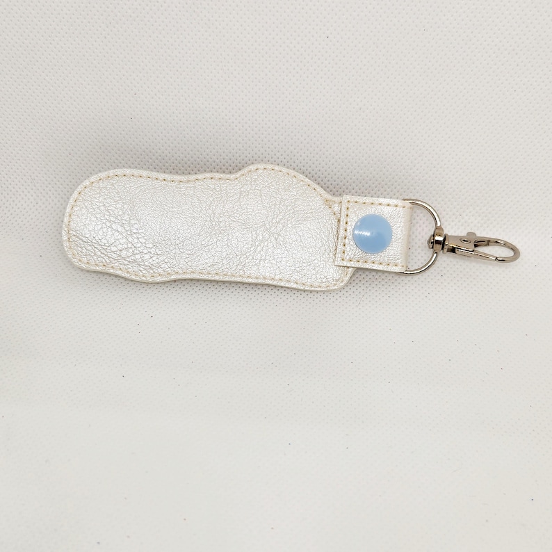 May include: A white leather keychain with a light blue button and a silver metal ring.