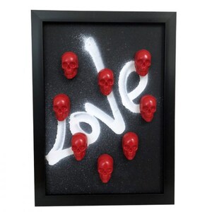 May include: Framed artwork with a black background and white spray paint that spells out the word "LOVE".  There are eight red skull figurines attached to the background.