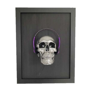 May include: A silver skull wearing purple headphones in a black frame.