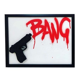 May include: A framed artwork featuring a black silhouette of a gun pointing at the word "BANG" in red spray paint.