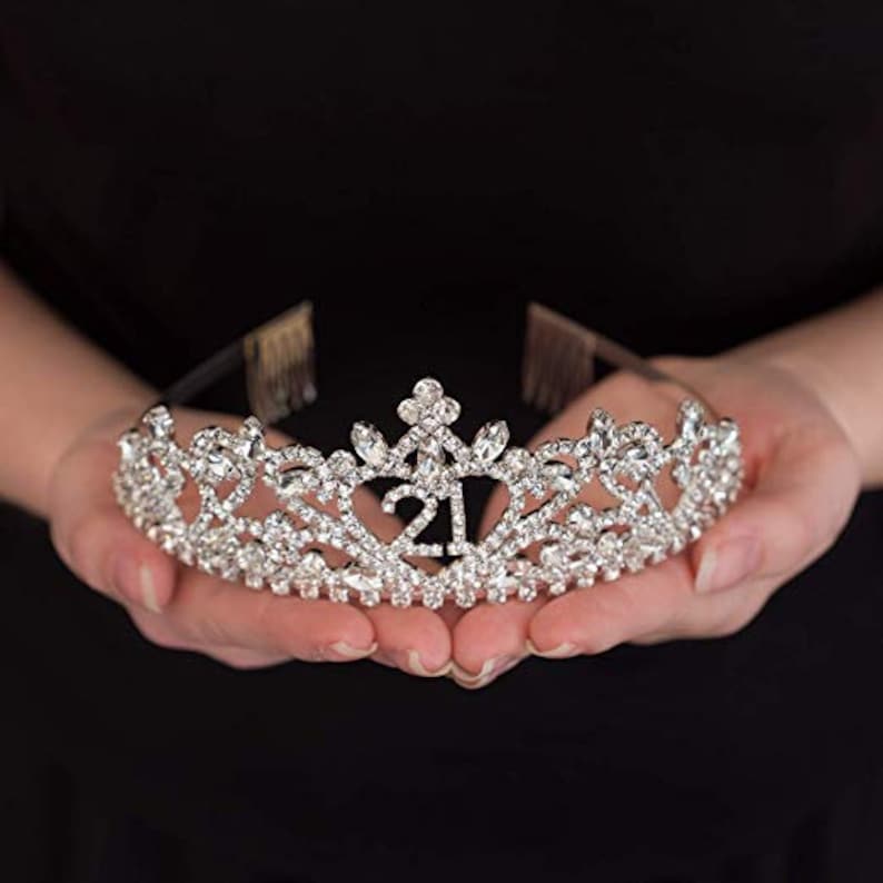 May include: A silver tiara with rhinestones and the number 21 in the center.