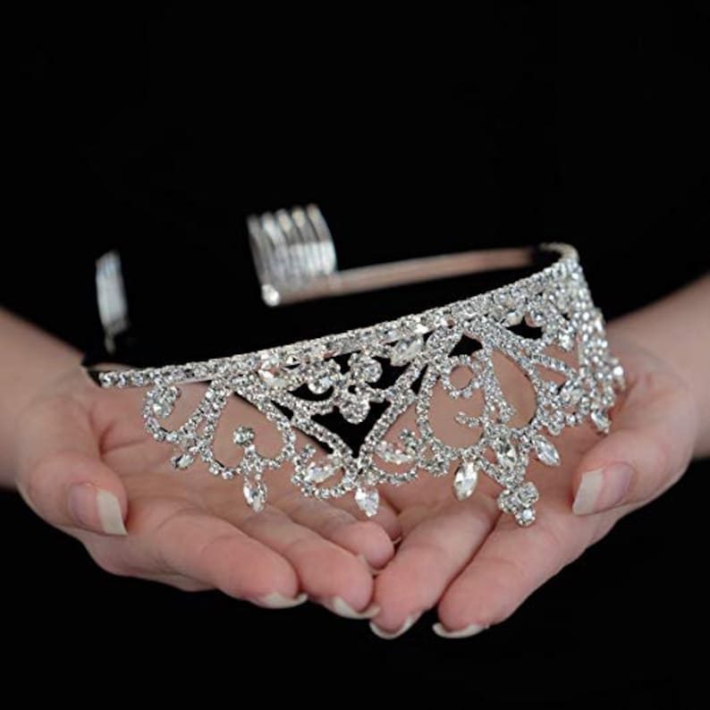 K&ouml;nnte beinhalten: Eine silberne Tiara mit einem zarten, filigranen Design, das mit klaren Strasssteinen besetzt ist. Die Tiara hat einen Kamm auf der R&uuml;ckseite, um sie leicht im Haar zu befestigen.