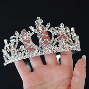 K&ouml;nnte beinhalten: Eine silberne Tiara mit einem filigranen Design und Strasssteinen. Die Tiara ist kronenf&ouml;rmig mit einer spitzen Spitze und einer geschwungenen Basis.