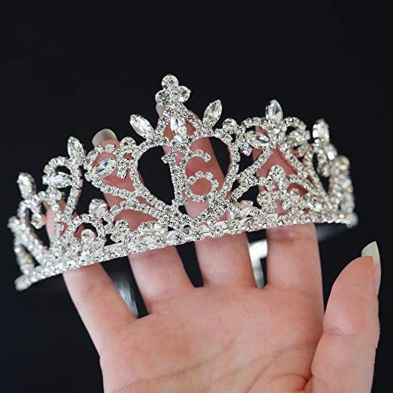 K&ouml;nnte beinhalten: Eine silberne Tiara mit einem filigranen Design und Strasssteinen. Die Tiara ist kronenf&ouml;rmig mit einer spitzen Spitze und einer geschwungenen Basis.