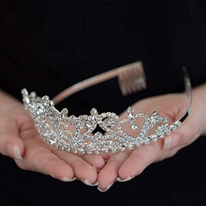K&ouml;nnte beinhalten: Eine silberne Tiara mit einem zarten Design, das mit klaren Strasssteinen besetzt ist. Die Tiara hat einen Kamm auf der R&uuml;ckseite f&uuml;r einfaches Einsetzen in das Haar.