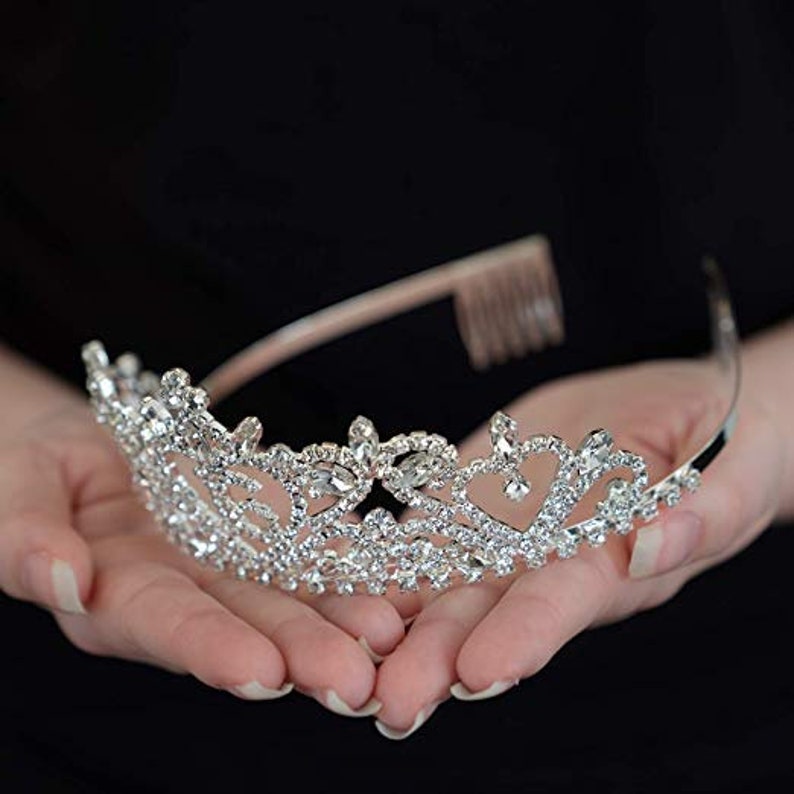 K&ouml;nnte beinhalten: Eine silberne Tiara mit einem zarten Design, das mit klaren Strasssteinen besetzt ist. Die Tiara hat einen Kamm auf der R&uuml;ckseite f&uuml;r einfaches Einsetzen in das Haar.