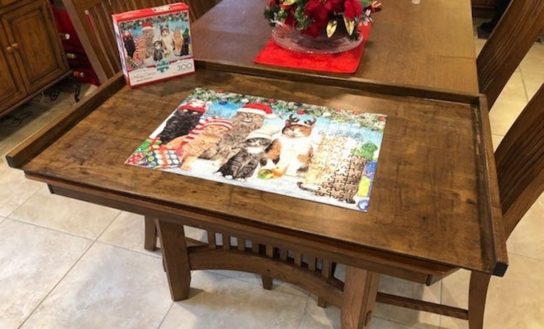 May include: A wooden puzzle table with a raised edge to keep puzzle pieces from falling off. A completed Christmas cat puzzle is on the table. The puzzle features cats wearing Santa hats and reindeer antlers.
