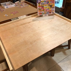 May include: A wooden jigsaw puzzle board with a light wood frame. The board is empty and ready for a puzzle.