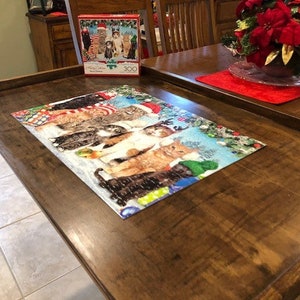 May include: A wooden jigsaw puzzle table with a completed cat jigsaw on top. The puzzle features a group of cats wearing Santa hats and scarves. The table has a dark brown finish and a raised edge to keep the jigsaw pieces from falling off.