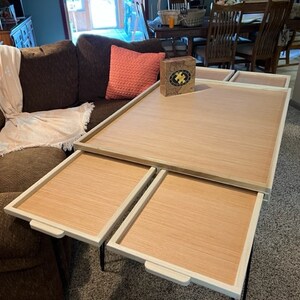 May include: A wooden coffee table with four removable trays. The table is white with a wood grain top. The trays are also white with a wood grain top. The table is sitting on a light grey carpet.