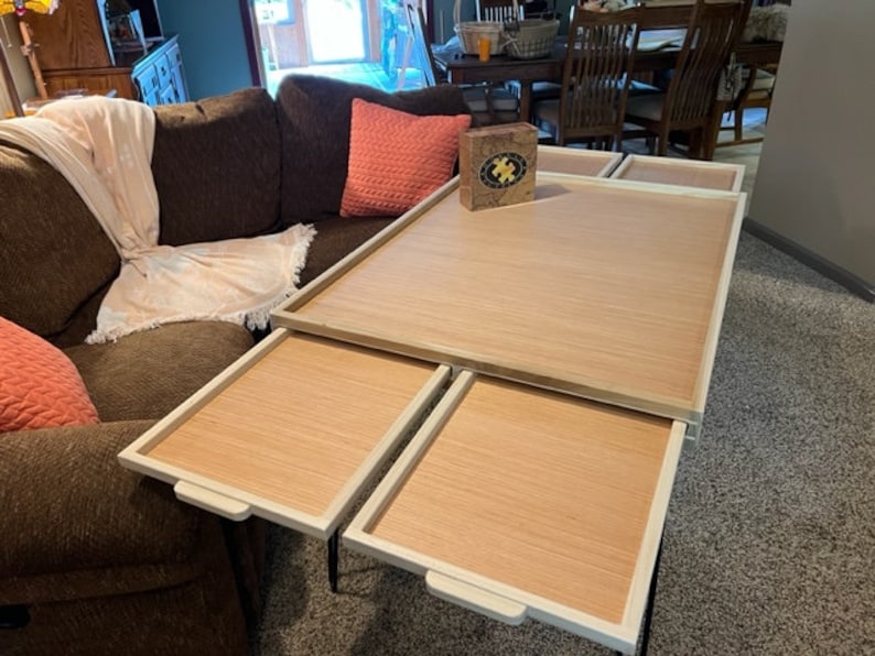 May include: A wooden coffee table with four removable trays. The table is white with a wood grain top. The trays are also white with a wood grain top. The table is sitting on a light grey carpet.