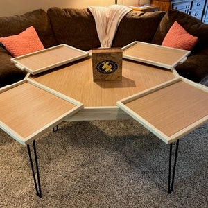 May include: A hexagonal coffee table with four removable trays. The table has a light wood finish and black hairpin legs. A wooden puzzle box sits in the centre of the table.