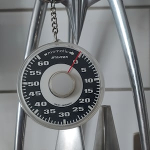 Può includere: Uno strumento da cucina argentato con un quadrante rotondo nero che riporta la scritta "mematic STAIGER" e numeri da 0 a 60. Il quadrante ha un ago rosso che punta al numero 0.