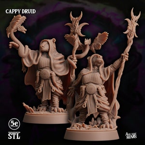 May include: Two 3D printed miniature figures of a Cappy Druid, a humanoid creature with a capybara-like head, wearing a robe and holding a staff. The figures are painted in a brown color and are standing on a base.