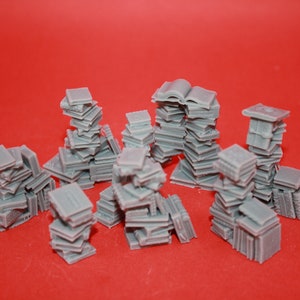 May include: A collection of gray miniature stacks of books, some with open pages, arranged on a red surface.