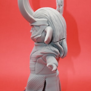 May include: A grey plastic figurine of a character with horns, a long flowing cape, and a detailed face. The figurine is standing on a black base.