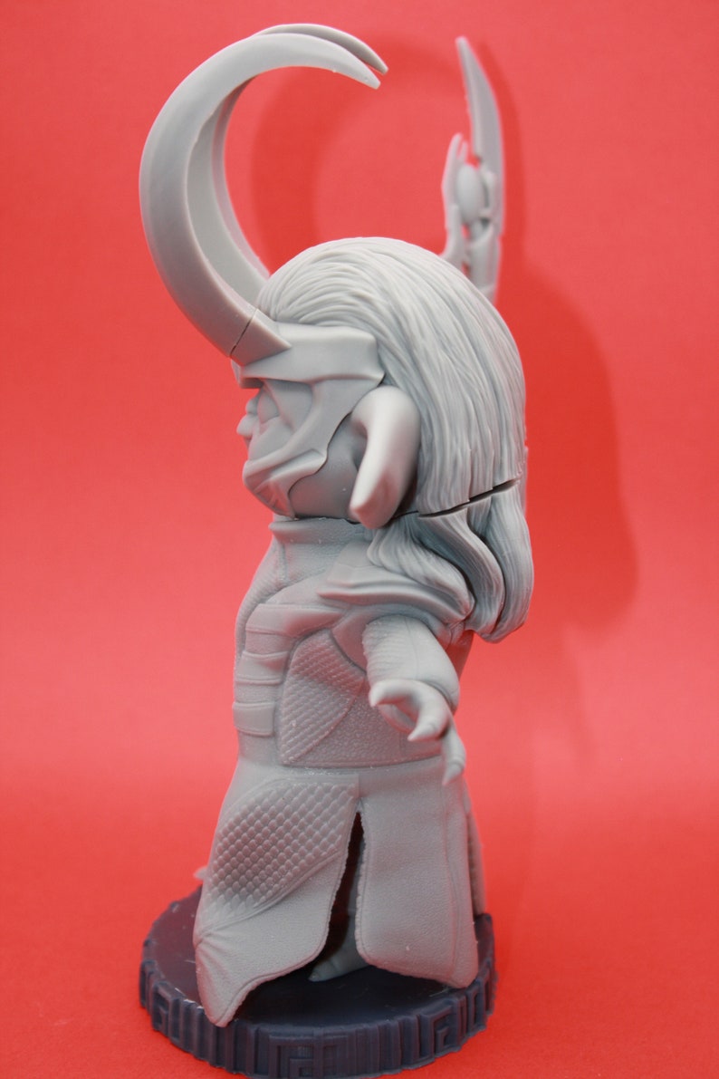 May include: A grey plastic figurine of a character with horns, a long flowing cape, and a detailed face. The figurine is standing on a black base.