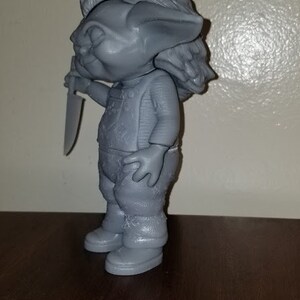K&ouml;nnte beinhalten: Eine graue 3D-gedruckte Figur eines Trolls, der ein Messer h&auml;lt. Der Troll hat einen schelmischen Ausdruck und tr&auml;gt ein Hemd und eine Hose.
