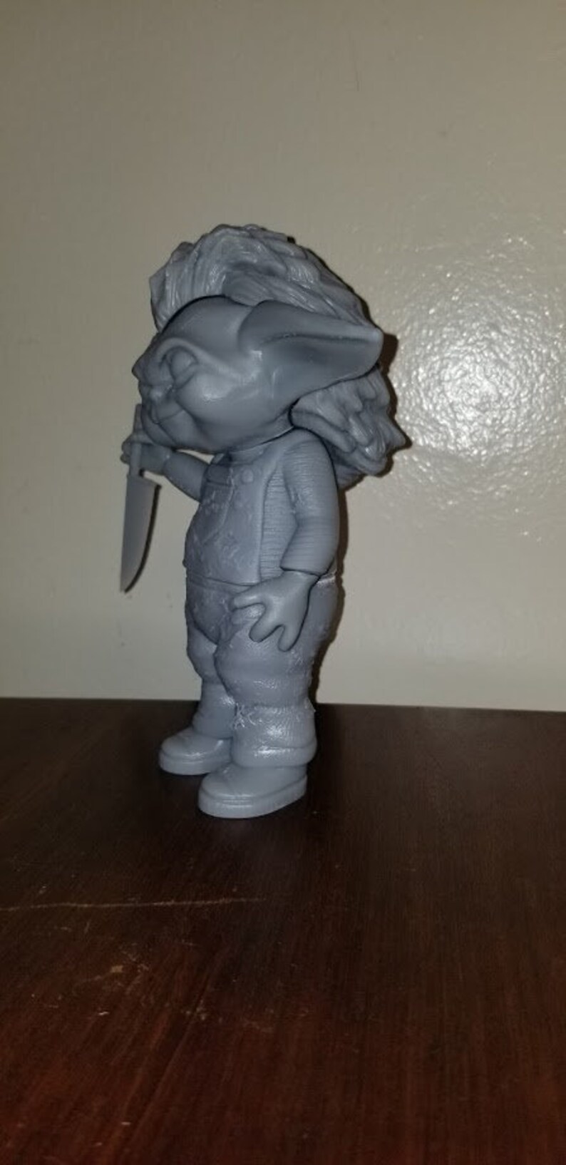 K&ouml;nnte beinhalten: Eine graue 3D-gedruckte Figur eines Trolls, der ein Messer h&auml;lt. Der Troll hat einen schelmischen Ausdruck und tr&auml;gt ein Hemd und eine Hose.