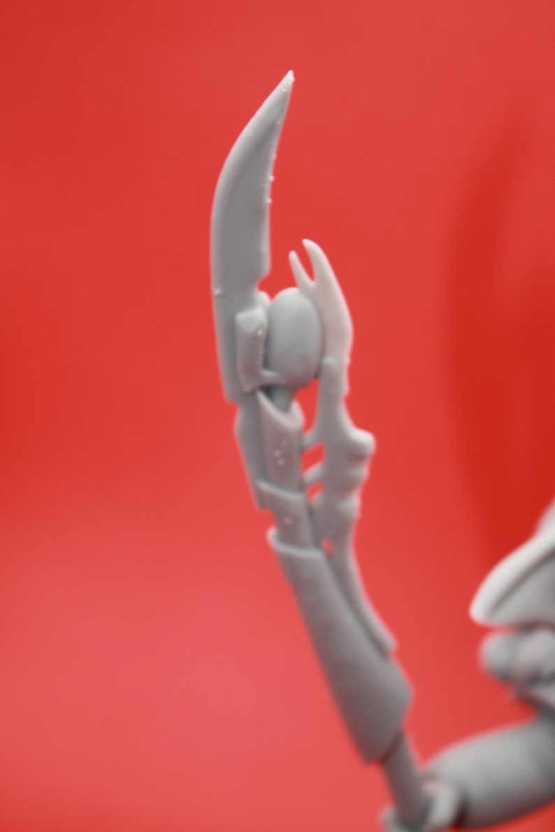 May include: A close-up of a grey plastic model of a weapon with a sharp point and intricate details. The weapon is designed with a futuristic, sci-fi aesthetic.