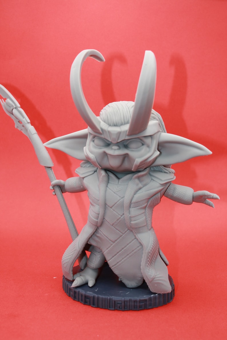 May include: A grey 3D printed figurine of a character with horns, a long robe, and a staff. The character is standing on a round base.