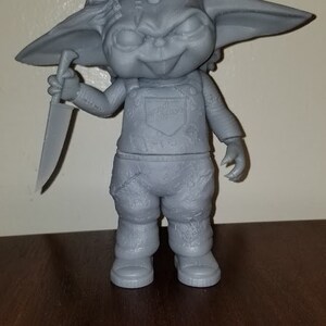 K&ouml;nnte beinhalten: Eine graue 3D-gedruckte Figur eines kleinen Wesens mit gro&szlig;en Ohren, einem verschmitzten Grinsen und einem Messer in der Hand. Das Wesen tr&auml;gt eine Latzhose und hat eine unordentliche Frisur.