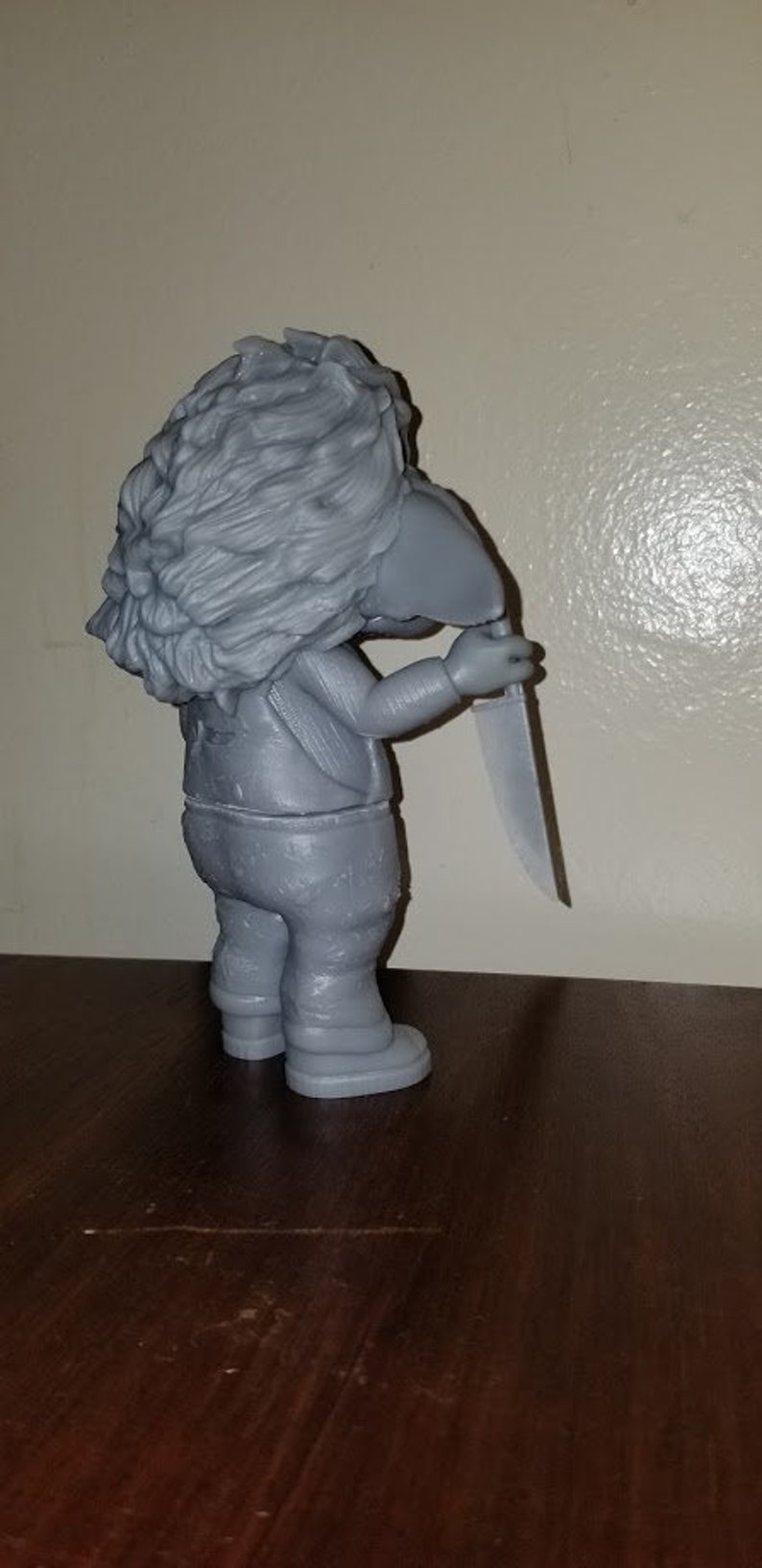 K&ouml;nnte beinhalten: Eine graue 3D-gedruckte Figur eines Charakters mit einem Messer. Der Charakter hat einen pelzigen Kopf und tr&auml;gt eine Hose und eine Jacke.
