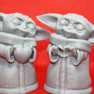 K&ouml;nnte beinhalten: Zwei graue 3D-gedruckte Figuren eines beliebten fiktiven Charakters, eine h&auml;lt ein Herz und die andere formt mit ihren H&auml;nden ein Herz.