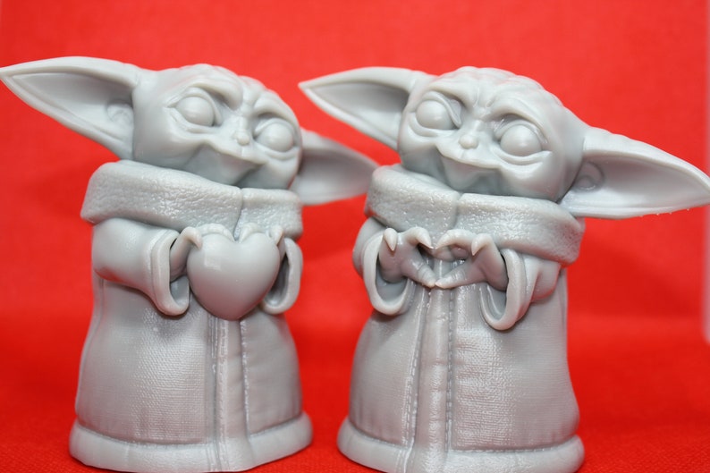 K&ouml;nnte beinhalten: Zwei graue 3D-gedruckte Figuren eines beliebten fiktiven Charakters, eine h&auml;lt ein Herz und die andere formt mit ihren H&auml;nden ein Herz.