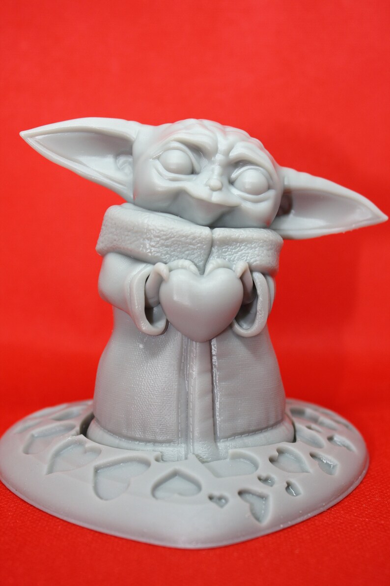 K&ouml;nnte beinhalten: Eine graue 3D-gedruckte Figur eines Charakters aus dem Star Wars-Franchise, die ein Herz in ihren H&auml;nden h&auml;lt. Die Figur steht auf einem herzf&ouml;rmigen Sockel.