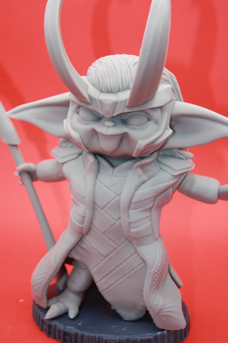 May include: A grey 3D printed figurine of a character with horns, a pointed hat, and a long robe. The character is holding a spear in its right hand and has a mischievous expression on its face.