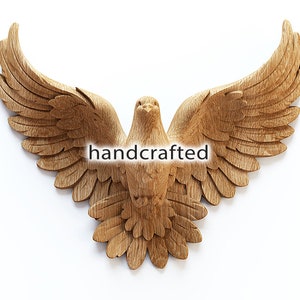 May include: A handcrafted wooden dove sculpture with outstretched wings. The bird is carved from light-colored wood, showcasing detailed feather textures. The word "handcrafted" is displayed across the center. A decorative piece for wall decor.