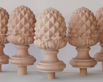 May include: Several unfinished wooden finials, each carved in the shape of a pineapple. The finials have a detailed, geometric pattern on the pineapple body and sit atop a decorative base. The wood has a natural, light brown color.