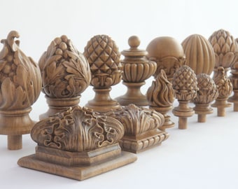 May include: A collection of intricately carved wooden finials in various shapes, including pineapples, floral designs, and spheres. The finials are displayed on a white background, showcasing their detailed craftsmanship and natural wood grain.