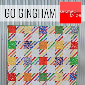 May include: A colorful quilt with a gingham pattern. The quilt is made up of squares of different colors and patterns, including red, yellow, green, blue, and white. The quilt is bordered in green fabric. The text "GO GINGHAM" is at the top of the image, and the text "seamed to be" is in a red box at the top right of the image.