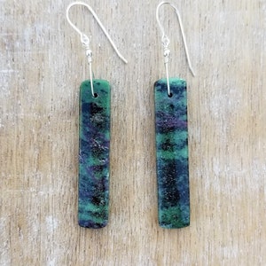 May include: A pair of silver dangle earrings with green, black and purple gemstone rectangular drops.