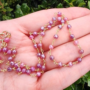 May include: A delicate gold chain necklace with pink faceted gemstone beads. The necklace is approximately 18 inches long and features a lobster clasp closure.