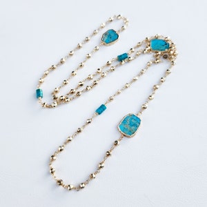 May include: A long gold chain necklace with turquoise stones. The chain is made of small, round beads and features three larger, irregular-shaped turquoise stones.