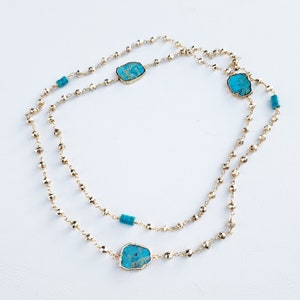 May include: A gold chain necklace with turquoise stones. The necklace is layered and has a delicate, beaded design.