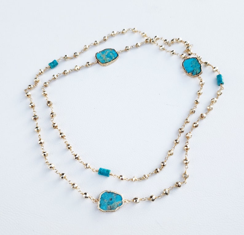 May include: A gold chain necklace with turquoise stones. The necklace is layered and has a delicate, beaded design.