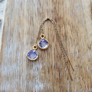 May include: A pair of gold dangle earrings with iridescent purple gemstone drops.